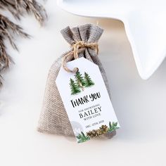 a thank you bag with pine trees on it next to a white plate and silverware