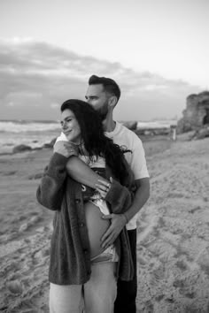 a man and woman standing next to each other on the beach with their arms around each other