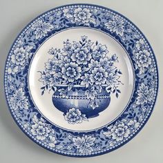 a blue and white plate with flowers in a vase on the bottom, against a gray background