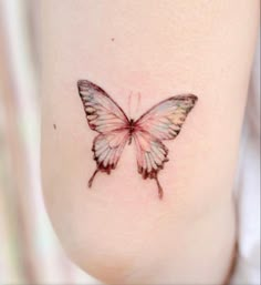 a small butterfly tattoo on the side of a woman's leg, it is pink and white