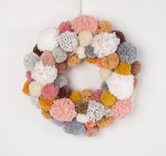 a multicolored knitted wreath hanging on a white door hanger with pom - poms