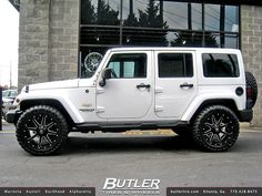 a white jeep is parked in front of a building with black rims and tires