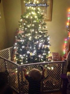 a small child is standing in front of a christmas tree with lights on it and looking down at the stairs