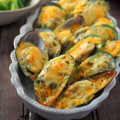 a dish filled with zucchini and cheese on top of a table next to bowls of salad