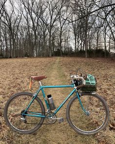 a blue bicycle parked in the middle of a field with trees and grass behind it