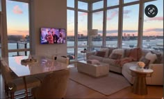 a living room filled with furniture and large windows overlooking the water at sunset or dawn