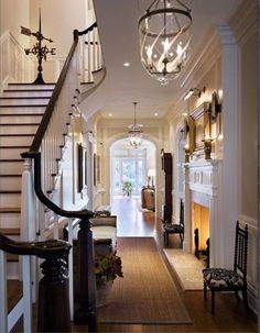 a hallway with stairs, chandelier and fireplace in the center is lit by two lights