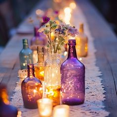 several bottles are lined up on a table with candles and flowers in the vases