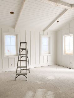 an empty room with a ladder in the middle and two windows on each side, all painted white