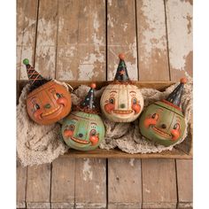 four painted pumpkins with faces on them sitting in a wooden box next to a rug