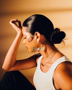 a woman sitting on the ground with her hands behind her head and wearing large earrings