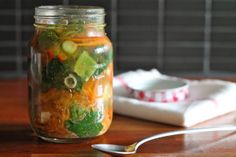 a mason jar filled with pickles, carrots and cucumbers next to a spoon