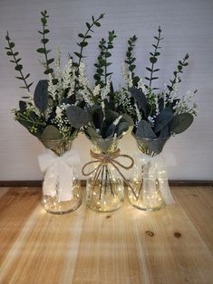 three vases with flowers and greenery in them