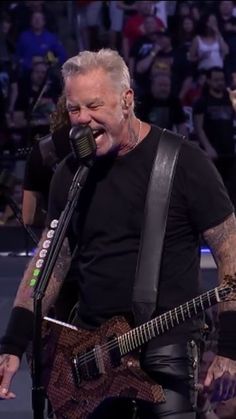 an image of a man singing into a microphone and playing guitar in front of a crowd