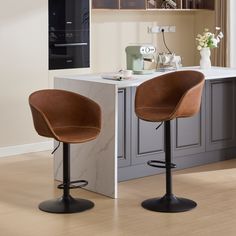 two brown bar stools sitting on top of a wooden floor next to a counter