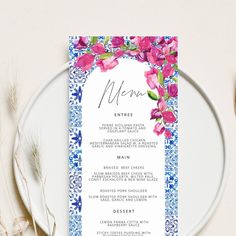 a white plate topped with a pink and blue floral menu card on top of a table