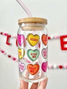 a hand holding a glass jar with hearts on it and a straw in the top