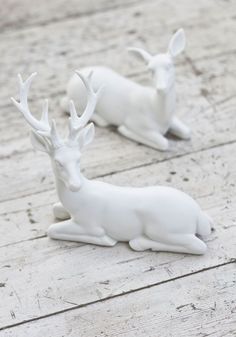 two white deer figurines sitting on top of a wooden floor next to each other