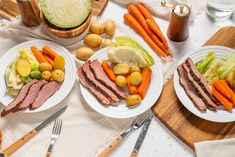 two white plates topped with meat and veggies on top of a wooden cutting board