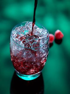 a glass filled with ice sitting on top of a table next to two cherries