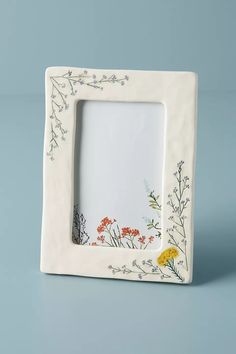 a white photo frame with flowers and leaves painted on the front, sitting on a blue surface