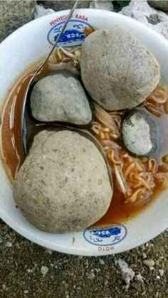 three rocks sitting in a bowl of noodles and meatballs with sauce on the side