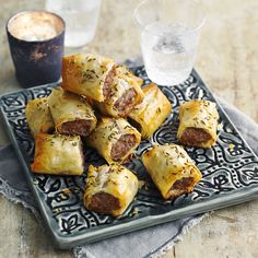 several sausage rolls on a plate next to a glass of water and a cup of tea