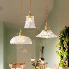 three lights hanging from the ceiling above a dining room table with flowers in vases