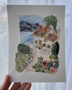 a hand holding up a piece of paper with a house on the hill in the background