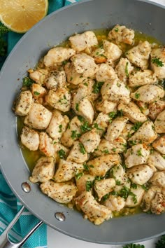 a skillet filled with chicken and garnished with parsley next to lemon wedges