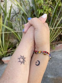 two people holding hands with sun and moon tattoos on their wrists, both wearing matching bracelets