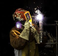 a man wearing a welding helmet and holding a grinder in his right hand with sparks coming out of it