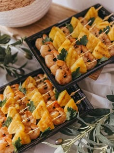 two trays filled with pineapple and shrimp skewers on top of a table