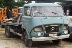 two old trucks parked next to each other in a yard with trees and machinery behind them