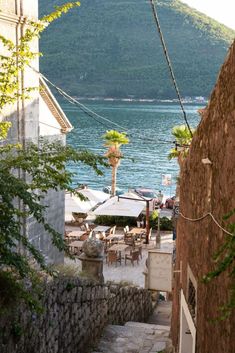 an alley way with tables and chairs next to the water in front of a mountain