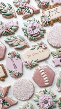 some decorated cookies are laying on a white tablecloth with name tags and flowers in pastel colors