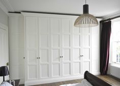 a bedroom with white closets and wood flooring next to a bed in front of a window