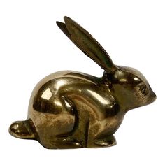 a gold colored metal rabbit figurine sitting on top of a white background,