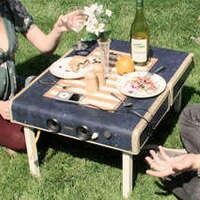 two people sitting on the grass eating food and drinking wine at an outdoor picnic table