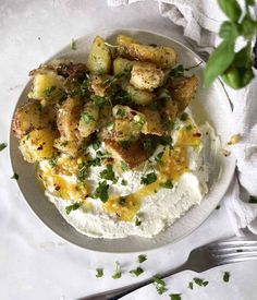 a white plate topped with mashed potatoes covered in cheese and parsley next to a fork