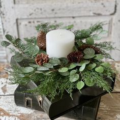 a candle is sitting on top of a box filled with greenery and pine cones