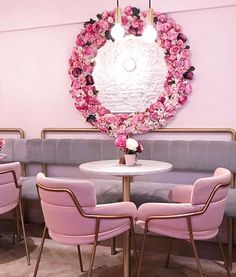 pink chairs are around a white table with a circular mirror on the wall behind it