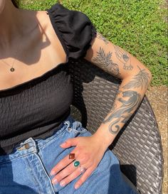 a woman with tattoos on her arm sitting in a chair next to a grass field