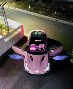 a pink car with wings on the hood parked in front of a building at night