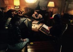 several people sitting around in a room with wooden tables and lamps on either side of them