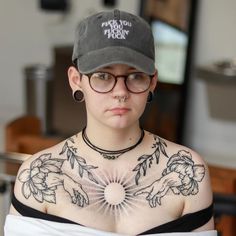 a woman with tattoos on her chest wearing glasses and a hat is looking at the camera