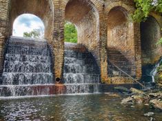 an old stone bridge with waterfall and arches over the water, surrounded by rocks and greenery