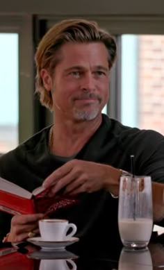 a man sitting at a table with a book in front of him and a cup of coffee