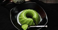 a black plate topped with a green donut next to a knife and bowl filled with cucumbers