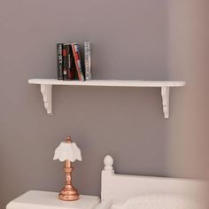 a white bed sitting under a shelf next to a lamp on top of a table